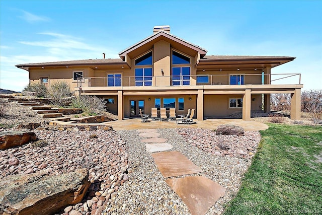 rear view of property with stucco siding, a chimney, a balcony, and a patio