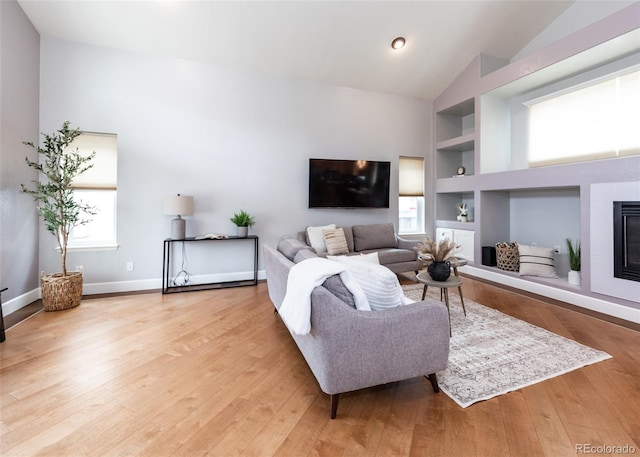 living area featuring built in features, vaulted ceiling, light wood-style flooring, and a fireplace