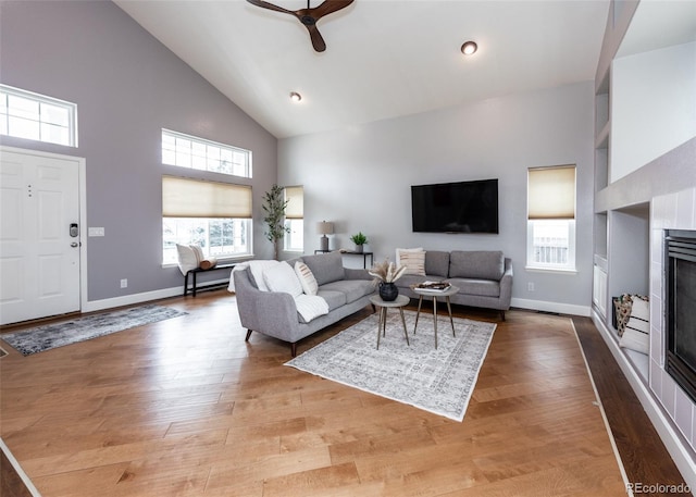 living room featuring a fireplace, baseboards, wood finished floors, and high vaulted ceiling