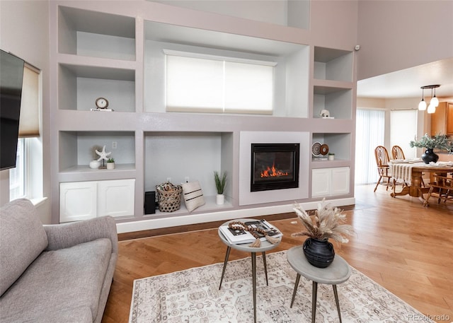 living room featuring built in features, a glass covered fireplace, and light wood-style flooring