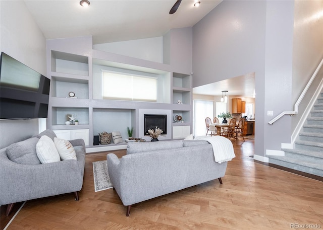 living area featuring a glass covered fireplace, built in features, baseboards, stairs, and light wood finished floors