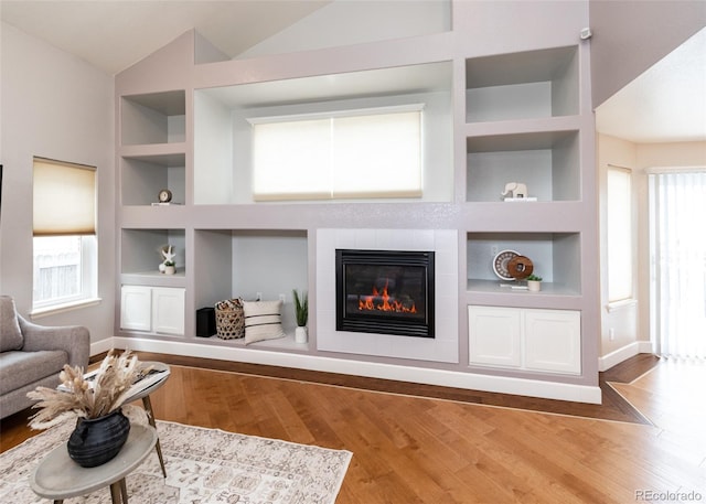 living room featuring a fireplace, vaulted ceiling, plenty of natural light, and built in features