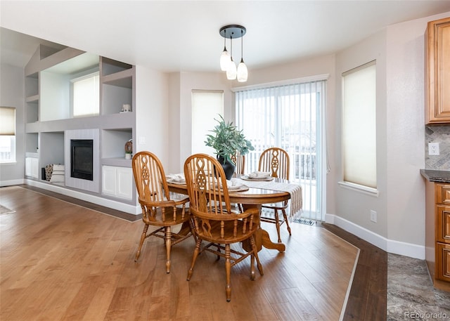 dining area with built in shelves, a glass covered fireplace, light wood-style floors, and baseboards