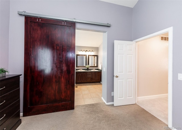 unfurnished bedroom with light carpet, baseboards, visible vents, and a barn door