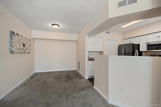 kitchen with stainless steel microwave, dark carpet, visible vents, freestanding refrigerator, and white cabinetry