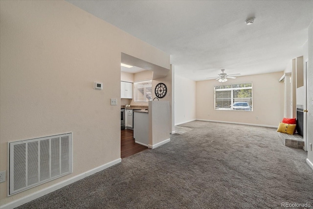 unfurnished living room featuring ceiling fan, dark carpet, visible vents, and baseboards