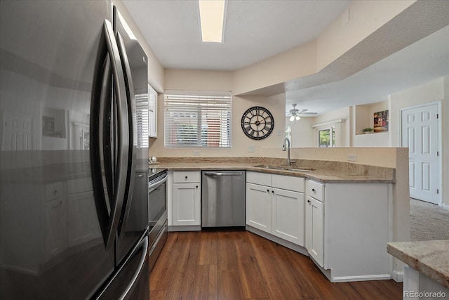 kitchen with dark wood finished floors, appliances with stainless steel finishes, a peninsula, white cabinetry, and a sink