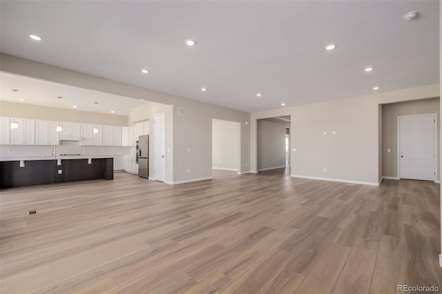56159 E Tomahawk Ave, Strasburg, CO 80136 - unfurnished living room featuring light wood-style flooring, recessed lighting, baseboards, and a sink