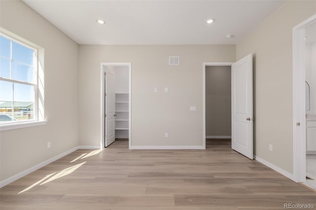 56159 E Tomahawk Ave, Strasburg, CO 80136 - unfurnished bedroom with light wood-type flooring, recessed lighting, a spacious closet, baseboards, and ensuite bath