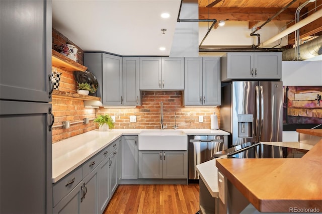 kitchen featuring open shelves, gray cabinets, stainless steel appliances, and a sink