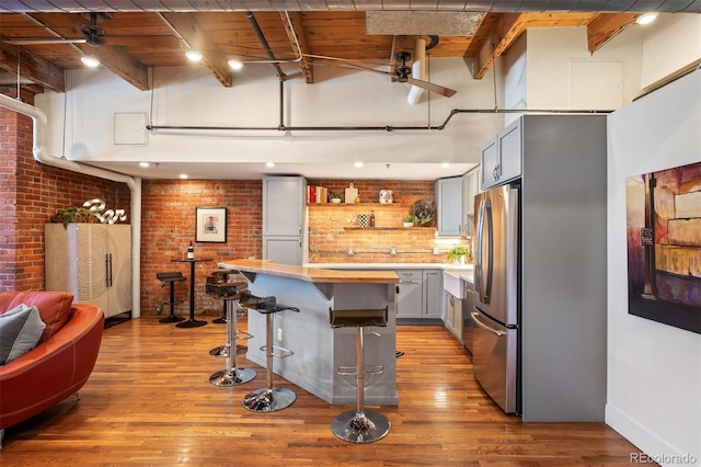 kitchen with open shelves, a high ceiling, freestanding refrigerator, beamed ceiling, and a kitchen breakfast bar