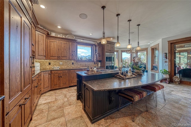 kitchen with a kitchen bar, a center island, hanging light fixtures, dark stone counters, and backsplash