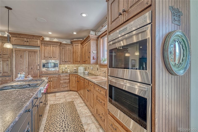 kitchen featuring sink, appliances with stainless steel finishes, decorative backsplash, decorative light fixtures, and dark stone counters