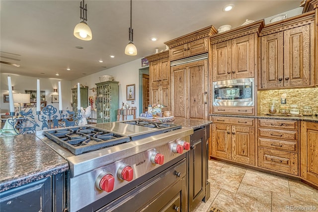 kitchen with appliances with stainless steel finishes, dark stone counters, hanging light fixtures, and backsplash