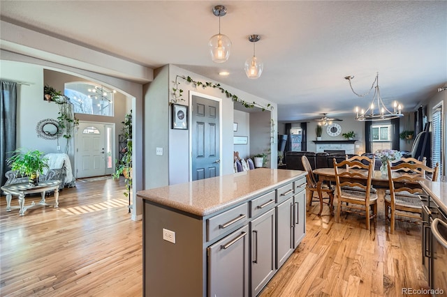 kitchen featuring ceiling fan with notable chandelier, a kitchen island, light wood-type flooring, and hanging light fixtures