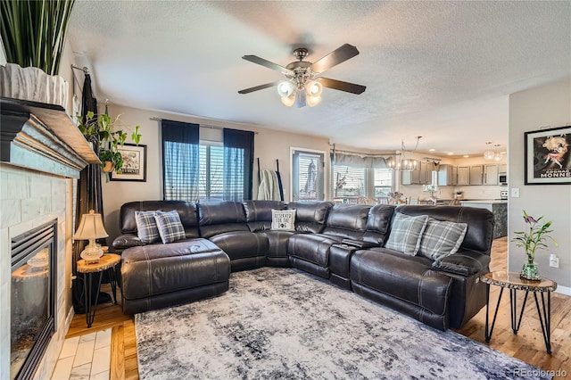 living room with ceiling fan with notable chandelier, a fireplace, light wood-type flooring, and a textured ceiling