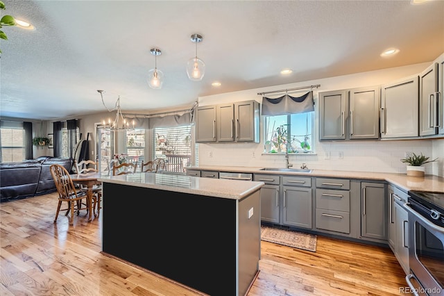 kitchen with sink, light hardwood / wood-style floors, hanging light fixtures, a kitchen island, and appliances with stainless steel finishes