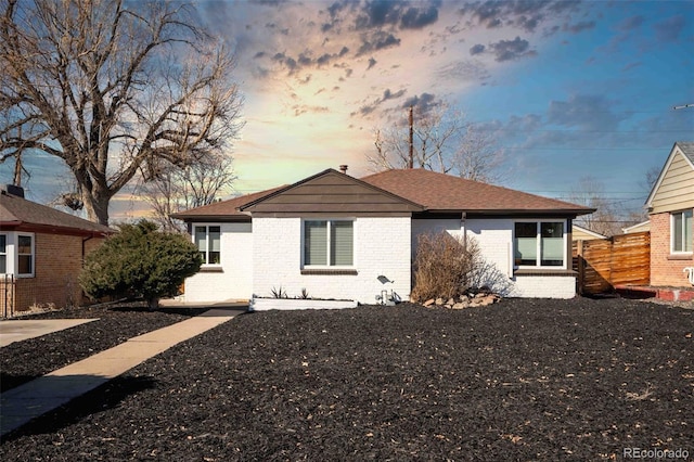 view of front facade featuring brick siding, fence, and roof with shingles