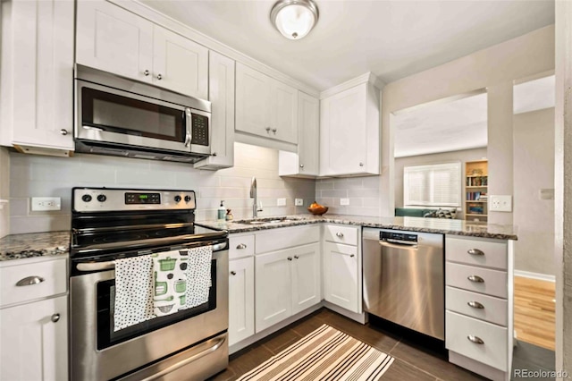 kitchen featuring light stone counters, stainless steel appliances, a sink, white cabinetry, and backsplash