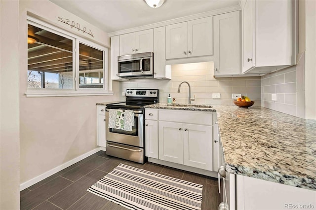 kitchen with a sink, white cabinetry, baseboards, appliances with stainless steel finishes, and tasteful backsplash