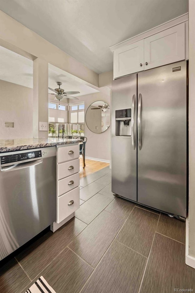 kitchen with stainless steel appliances, a ceiling fan, baseboards, white cabinets, and light stone countertops