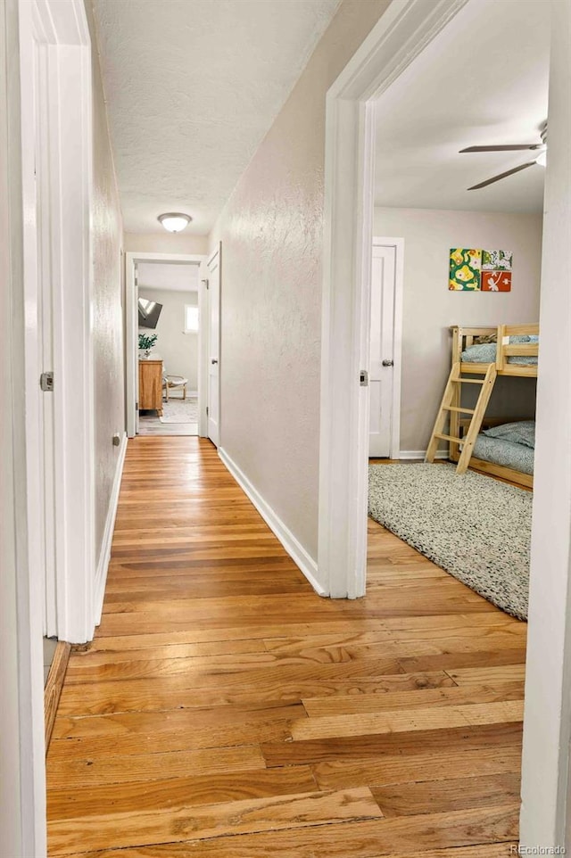 hallway featuring light wood finished floors, baseboards, and a textured wall