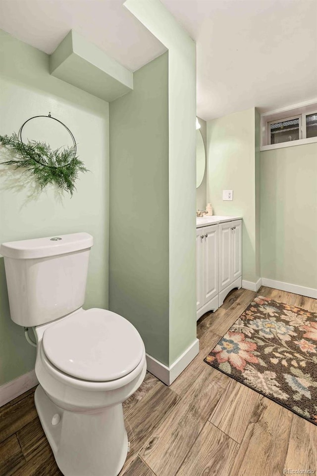 bathroom with toilet, baseboards, wood finished floors, and vanity