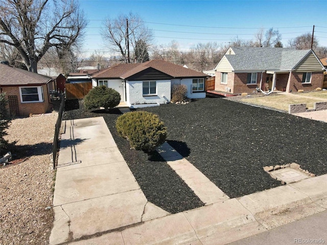 view of front of home featuring brick siding, fence, and roof with shingles