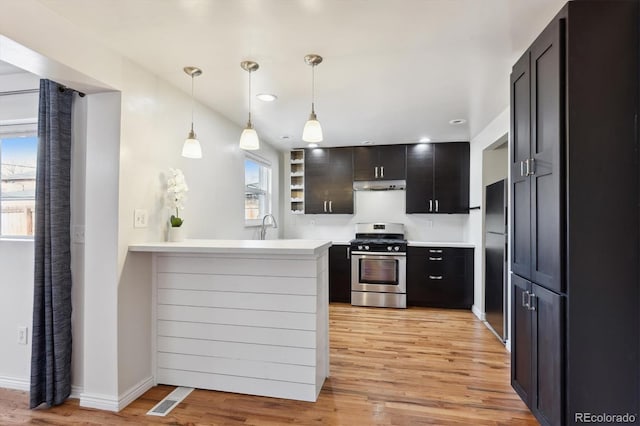 kitchen featuring under cabinet range hood, a peninsula, light wood-style floors, black fridge, and stainless steel gas stove