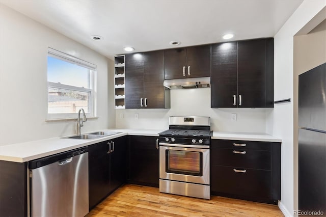 kitchen with light wood-style floors, stainless steel appliances, light countertops, under cabinet range hood, and a sink