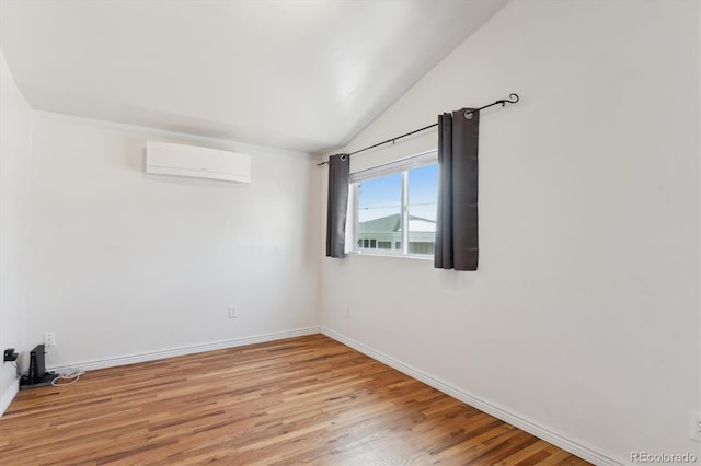 unfurnished room featuring lofted ceiling, a wall mounted AC, and light wood-type flooring