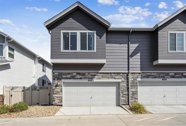 view of front of home featuring stone siding, a garage, concrete driveway, and fence