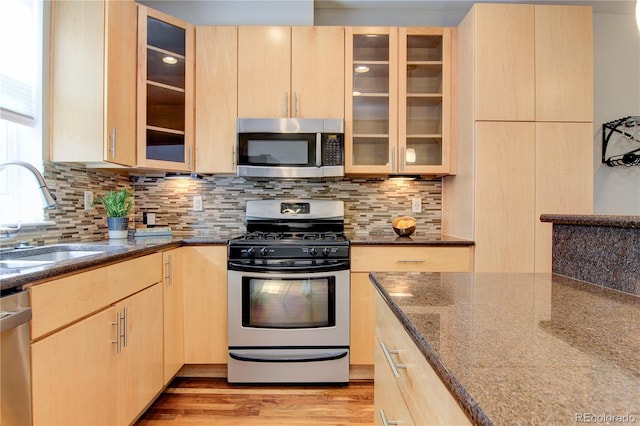 kitchen featuring appliances with stainless steel finishes, light brown cabinetry, sink, dark stone counters, and light hardwood / wood-style floors