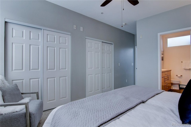 bedroom featuring connected bathroom, a baseboard heating unit, multiple closets, and ceiling fan