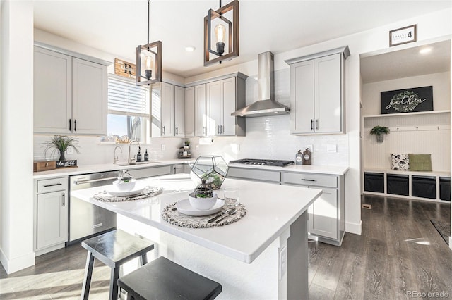 kitchen with sink, wall chimney exhaust hood, stainless steel appliances, dark hardwood / wood-style floors, and decorative light fixtures