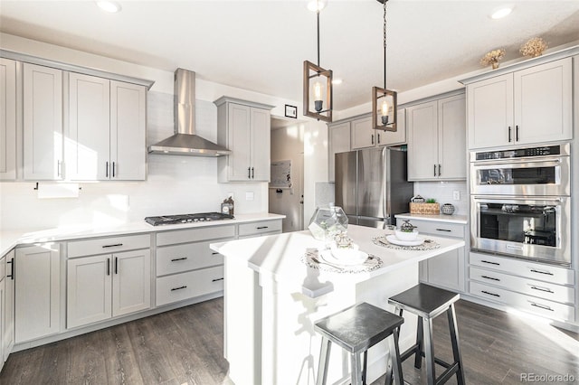 kitchen with wall chimney range hood, hanging light fixtures, dark hardwood / wood-style floors, gray cabinets, and appliances with stainless steel finishes