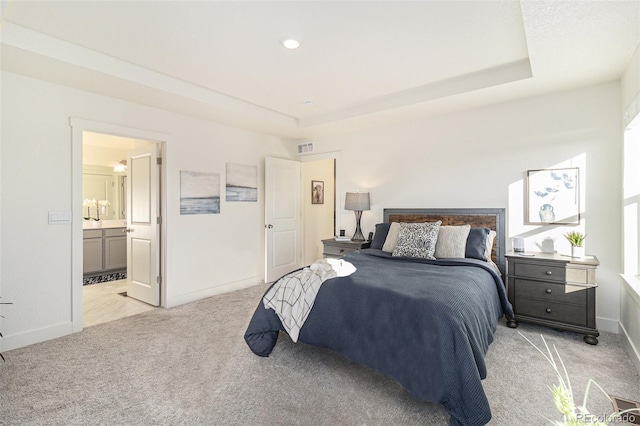 carpeted bedroom featuring a raised ceiling and ensuite bath