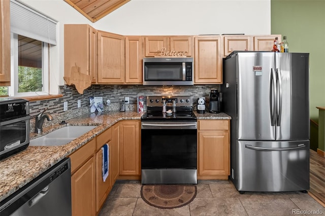 kitchen featuring a sink, stone countertops, lofted ceiling, tasteful backsplash, and appliances with stainless steel finishes