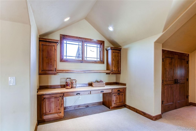 unfurnished office featuring built in desk, light colored carpet, and vaulted ceiling