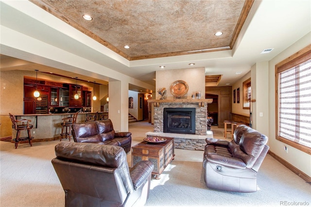 living room featuring a raised ceiling, a stone fireplace, and light colored carpet