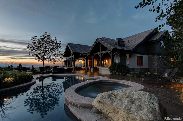 pool at dusk with an in ground hot tub and a patio