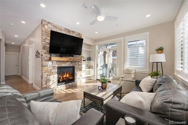 living room with plenty of natural light, light hardwood / wood-style floors, a stone fireplace, and ceiling fan