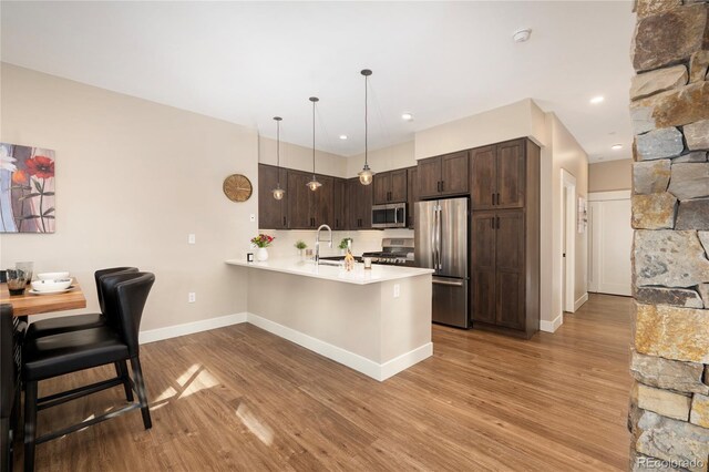 kitchen with decorative light fixtures, dark brown cabinets, light hardwood / wood-style floors, kitchen peninsula, and stainless steel appliances