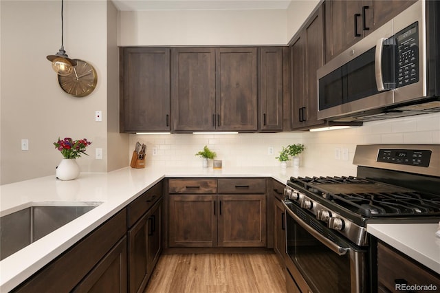 kitchen with dark brown cabinetry, stainless steel appliances, tasteful backsplash, decorative light fixtures, and light wood-type flooring