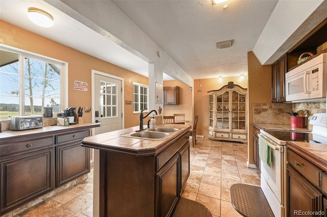 kitchen featuring white appliances, sink, a center island with sink, tasteful backsplash, and a textured ceiling