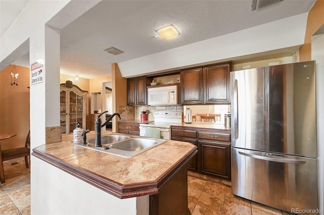 kitchen featuring white appliances, dark brown cabinets, tasteful backsplash, kitchen peninsula, and sink