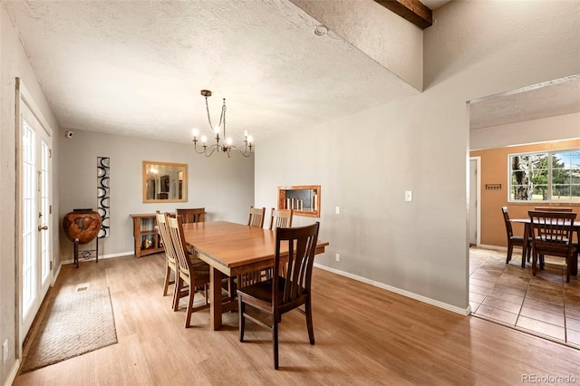 dining space featuring beam ceiling, a textured ceiling, an inviting chandelier, and light hardwood / wood-style floors