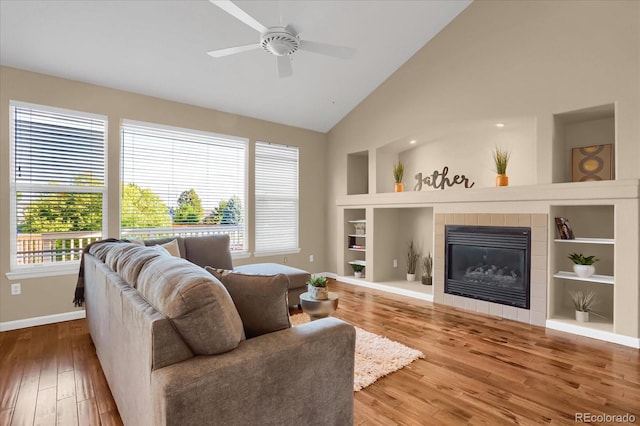 living room featuring built in shelves, ceiling fan, hardwood / wood-style floors, a fireplace, and vaulted ceiling