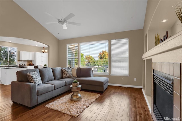 living room with ceiling fan with notable chandelier, high vaulted ceiling, dark hardwood / wood-style flooring, and a tile fireplace