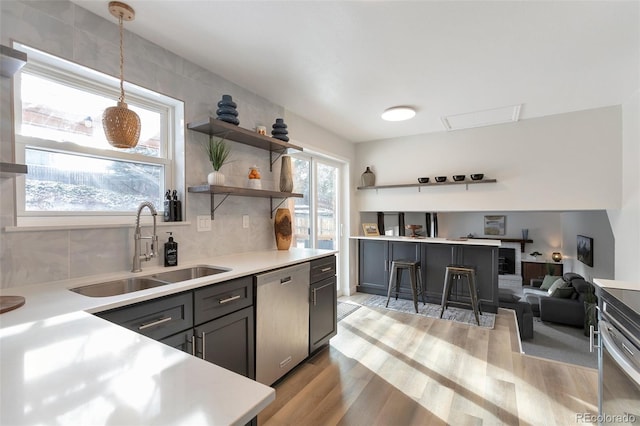 kitchen with dishwasher, sink, light hardwood / wood-style floors, decorative light fixtures, and a breakfast bar